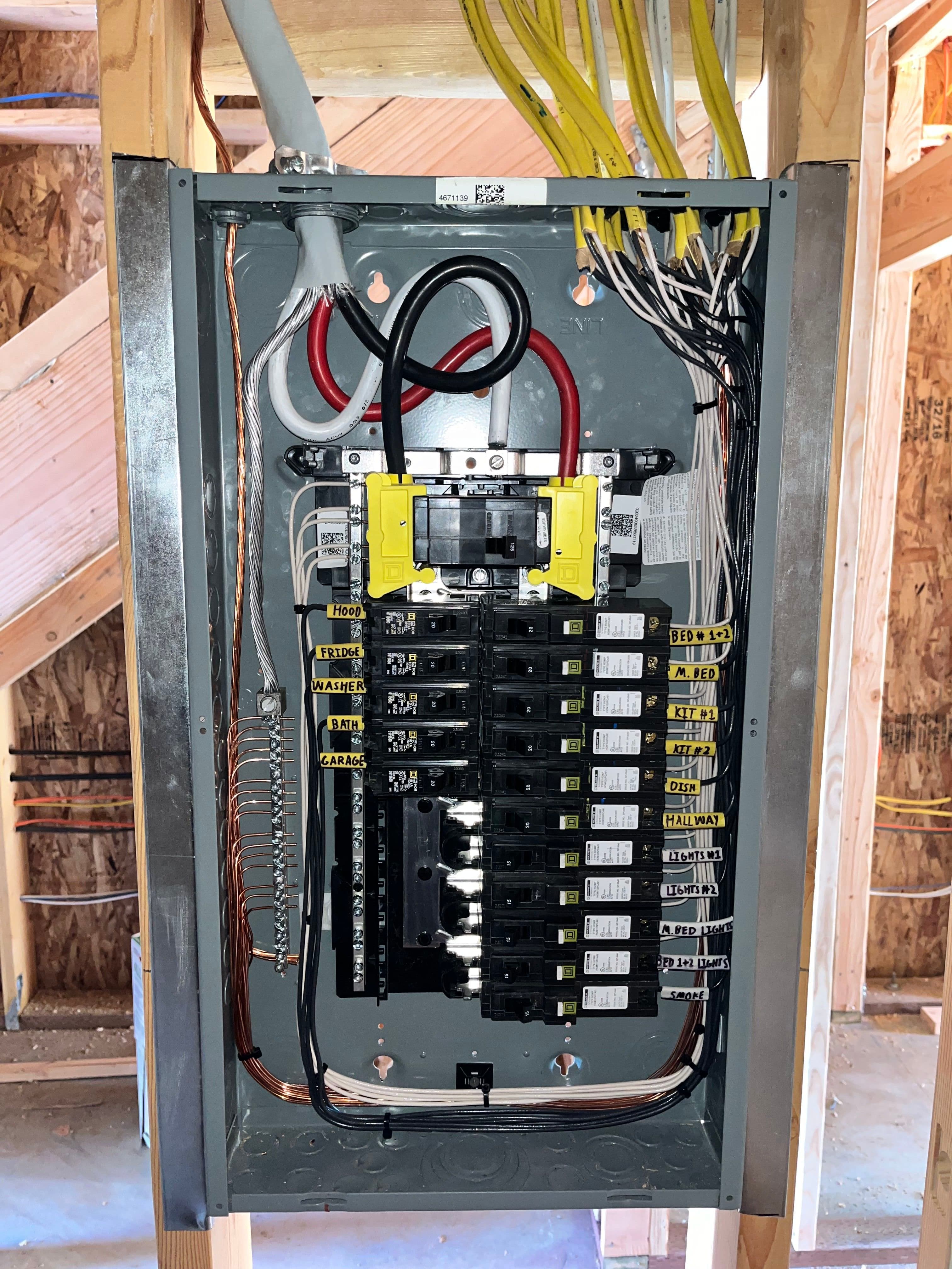 Electrical panel with circuit breakers and wiring in a residential construction setting.