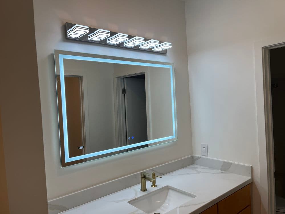 LED illuminated bathroom mirror with modern lighting above a sleek white countertop.